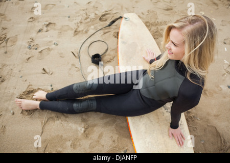 Lächelnd schöne Blondine im Neoprenanzug mit Surfbrett am Strand Stockfoto