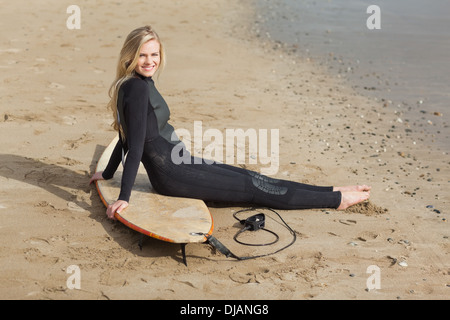 Porträt von einer Blondine im Neoprenanzug mit Surfbrett am Strand Stockfoto