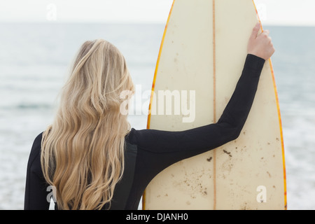 Rückansicht von einer Blondine im Neoprenanzug mit Surfbrett am Strand Stockfoto