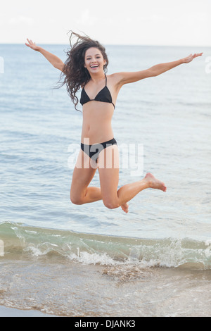 Fröhliche junge Frau im Bikini am Strand springen Stockfoto