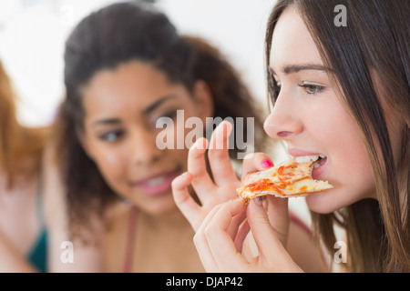 Junge Frau, die Pizza mit unscharfen Freunde zu Hause essen Stockfoto