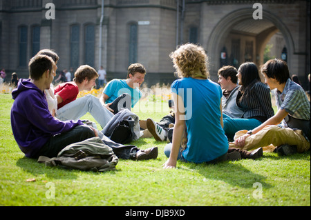 Gruppe von Multi Rasse Manchester Studenten saßen auf Rasen auf dem Campus im Sonnenschein reden und lachen, schauen glücklich Stockfoto