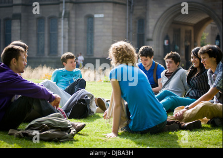 Gruppe von Multi Rasse Manchester Studenten saßen auf Rasen auf dem Campus im Sonnenschein reden und lachen, schauen glücklich Stockfoto