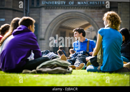 Gruppe von Multi Rasse Manchester Studenten saßen auf Rasen auf dem Campus im Sonnenschein reden und lachen, schauen glücklich Stockfoto