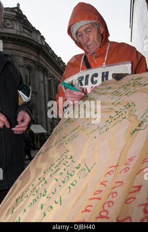 London, UK. 26. November 2013. . Ein Demonstrant fügt hinzu, dass seine Botschaft zu einem Sarg-förmigen Plakat als Brennstoff Armut Action, besetzen London und behinderten Menschen gegen Kürzungen Protest vor dem Sitz der Npower gegen scharfe Energie-und Heizkosten und eine angebliche 31.000 Todesfälle infolge Energiearmut steigt. Bildnachweis: Paul Davey/Alamy Live-Nachrichten Stockfoto