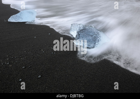 Eisblock an einem Strand mit Lavasteinen und Wasser schwebend über. Stockfoto