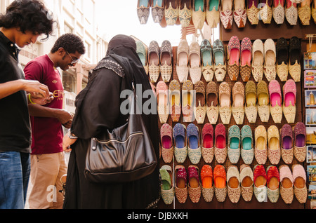 Arabische Frau, die eine Burka tragen haggles mit einem Anbieter verkaufen traditionelle indische Schuh in Bur Dubai Souk. Dubai, Vereinigte Arabische Emirate. Stockfoto