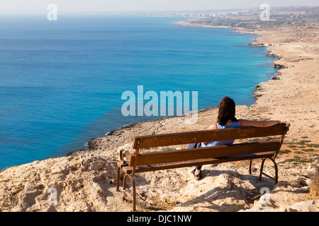 Frau sitzt auf einer Bank mit Blick auf Ayia Napa von der Landzunge Klippe am Kap Grecko, Zypern. Stockfoto