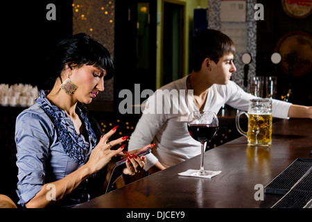 Stilvolle junge Frau sitzen an der Theke an der Bar senden eine Sms-Nachricht auf ihr Handy, Seitenansicht Stockfoto