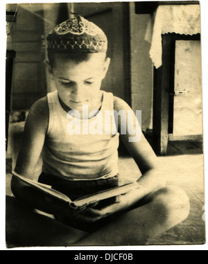 Junge in Shorts, T-shirt und Helmkraut ein Buch lesen, sitzen auf dem Boden, UdSSR, 1950er Jahre Stockfoto