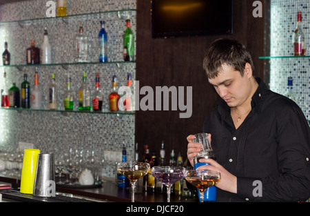 Barkeeper in einem Pub Vorbereitung alkoholische Cocktails stehen hinter der Theke mischen Getränke in drei eleganten cocktail-Gläser Stockfoto