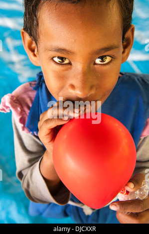 Rosivula, eine 6 jährige Schülerin (in ihrer Uniform) bläst einen Ballon ein Tourist (ein Seglerherz) ihr gegeben hatte. Fulaga, Laus, Fidschi Stockfoto