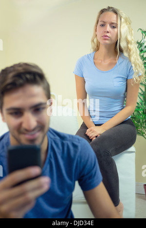 Lächelnder junge Mann mit seinem Smartphone im Wohnzimmer Stockfoto