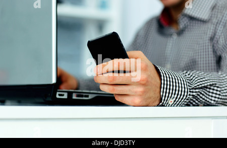 Nahaufnahme der männlichen Hand holding Smartphone und auf einer Laptoptastatur tippen Stockfoto