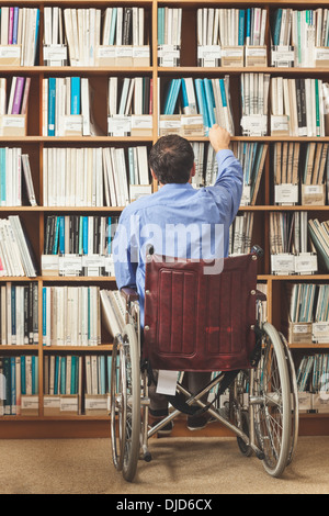 Mann im Rollstuhl setzen wieder ein Buch im Bücherregal Stockfoto