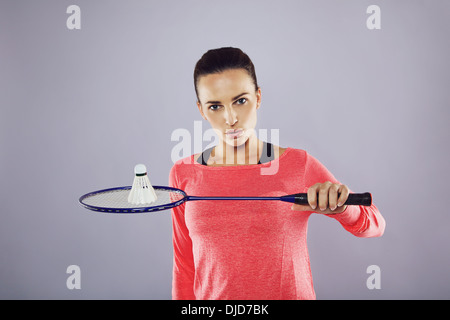 Porträt von zuversichtlich junges Mädchen hält einen Badminton-Schläger mit Federball Blick in die Kamera vor grauem Hintergrund. Stockfoto