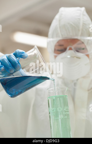 Laborantin mit Maske blaue Flüssigkeit im Becherglas gießen Stockfoto