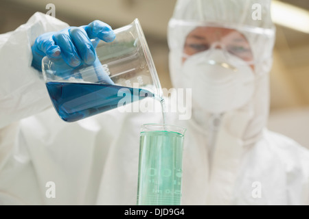 Laborantin mit Maske mischen blaue Flüssigkeit im Becherglas Stockfoto