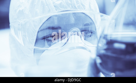 Laborantin mit Maske eng mit Blick auf Flüssigkeit Stockfoto