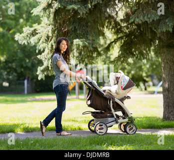 Junge Mutter schieben Kinderwagen im Park Stockfoto