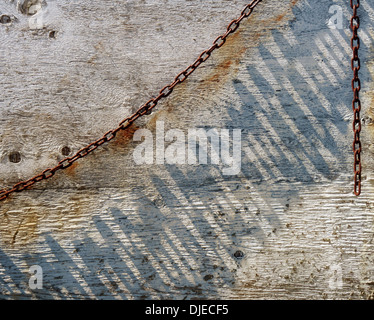 Ein verrosteter Bogen der Kette lässt lange Schatten auf eine alte bemalte Wand Dank der Winkel von der Mittagssonne Zeit skimming über ihn. Stockfoto