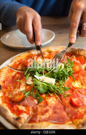 Mann unter Stück San Daniele Pizza mit Rucola und Prosciutto Stockfoto