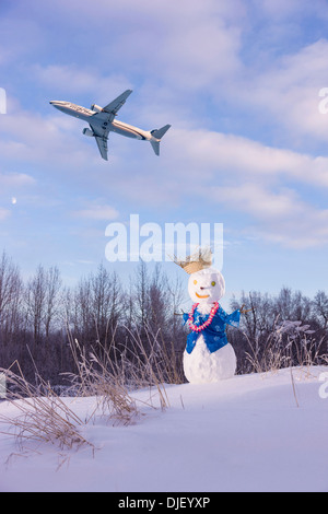 Zusammensetzung: Alaska Airlines Jet am Himmel über einen Schneemann tragen einen hawaiianischen Outfit Ted Stevens International Flughafen Stockfoto