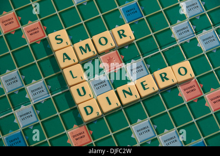 Die spanische Phrase, "Salud Amor y Dinero" (Gesundheit, Liebe und Geld) in Scrabble Fliesen auf einem Scrabble-Brett geschrieben. Stockfoto