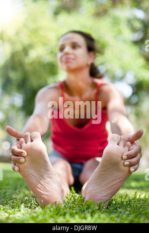 Lächelnde junge Frau sitzt auf dem Rasen. Das Gesicht in Unschärfe. Stockfoto