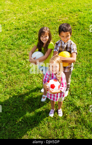 Drei glückliche Kinder, jungen und Mädchen stehen im sonnigen Sommerpark hält Sport Kugeln, Ansicht von oben Stockfoto