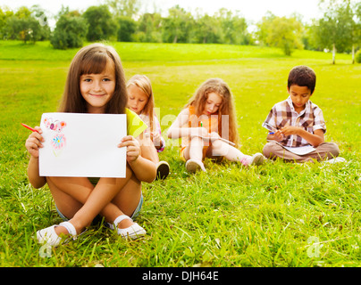 Niedliche kleine siebenjährige Mädchen zeichnen im Park draußen sitzen auf dem Rasen Stockfoto