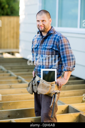 Arbeiter mit Digital-Tablette und Hammer im Werkzeuggürtel am Standort Stockfoto