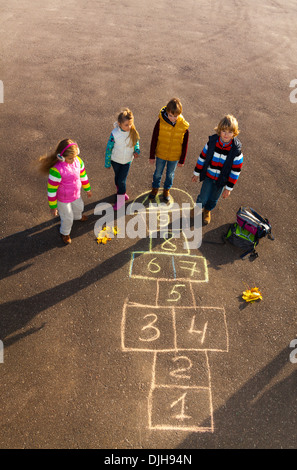 Gruppe von Kinder springen auf dem Himmel und Hölle Spiel gezogen auf dem Asphalt nach der Schule nach der Schule im Herbst Kleidung Stockfoto