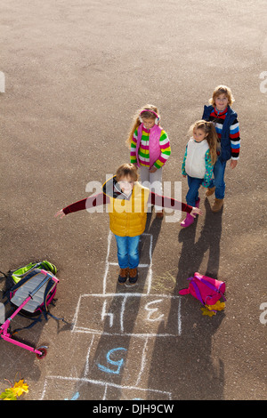 Junge, springen über Himmel und Hölle Spiel mit Freunden Jungs ein Mädchen Herbst Kleidung mit Schultaschen, die Verlegung in der Nähe von Standby Stockfoto