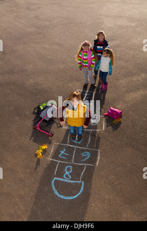 Junge, springen über Himmel und Hölle Spiel mit Kumpels Jungs ein Mädchen mit Schultaschen, die Verlegung in der Nähe von Standby Stockfoto