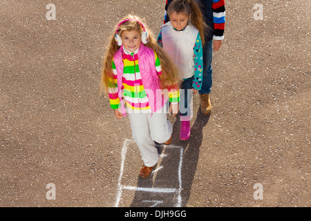 Gruppe von Kindern spielen im Freien mit Mädchen mit langen Haaren, die springen auf Himmel und Hölle Stockfoto