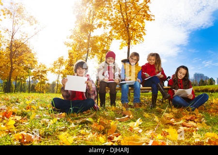 Gruppe von fünf Kinder Zeichnung Bilder sitzen auf der Bank im Herbst Park unter den Ahornbäumen Stockfoto