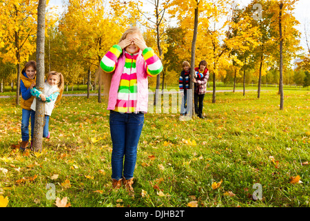 Gruppe von fünf Kinder spielen hide and seek mit Mädchen zählen und Freunde versteckt hinter den Bäumen Stockfoto