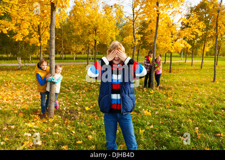 Gruppe von fünf Kinder spielen hide and seek mit jungen zählen und Freunde versteckt hinter den Bäumen Stockfoto