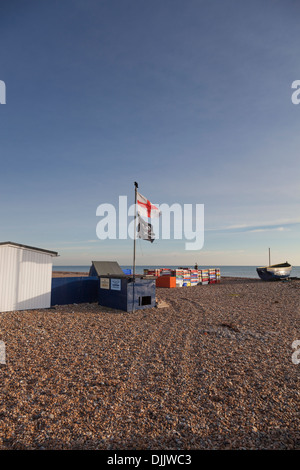 Flagge von St. George und der "Jolly Roger" Piratenflagge fliegen auf einem Kiesstrand inmitten von Fisch-Container und ein Fischerboot. Stockfoto