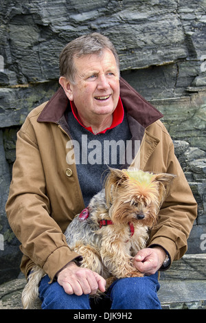 Reifer Mann, sitzen in der Nähe von Felsen am Strand, mit seinem Haustier Yorkshire Terrier Hund auf dem Schoß, Harlyn Bay, Padstow, Cornwall, Englan Stockfoto