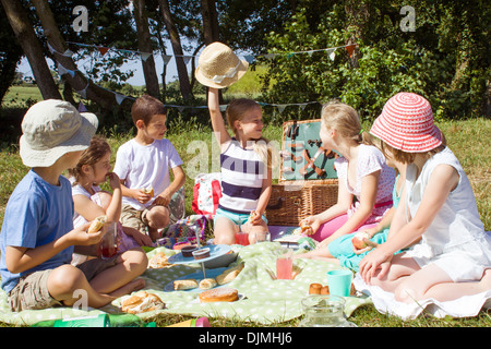 sieben Kinder sitzen mit einem Picknick, sitzen auf einer Decke Essen in Somerset, Großbritannien. Stockfoto