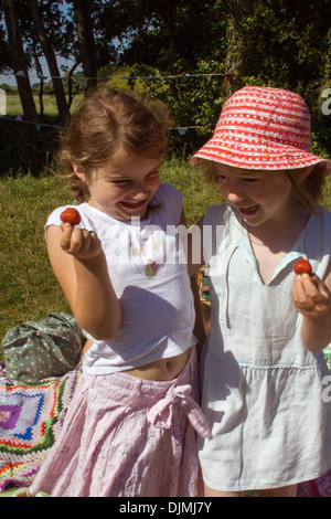 Zwei junge Mädchen Lachen und Spaß, auf ein Picknick in der Sonne, Erdbeeren halten und Spaß in Somerset, Großbritannien. Stockfoto