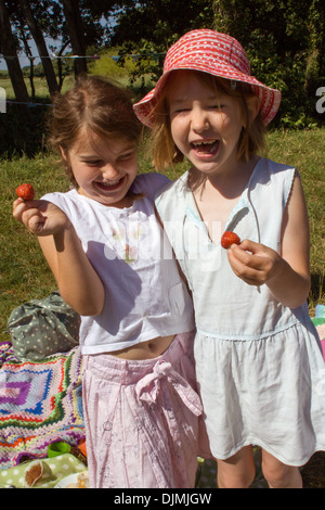 Zwei junge Mädchen Lachen und Spaß, auf ein Picknick in der Sonne, Erdbeeren halten und Spaß in Somerset, Großbritannien. Stockfoto