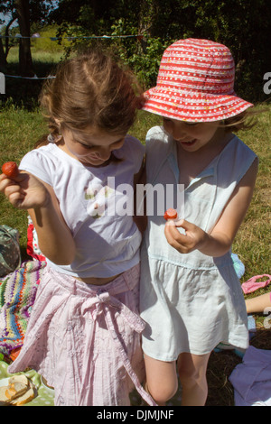 Zwei junge Mädchen Lachen und Spaß, auf ein Picknick in der Sonne, Erdbeeren halten und Spaß in Somerset, Großbritannien. Stockfoto