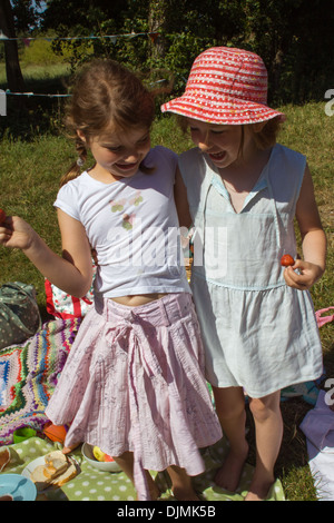 Zwei junge Mädchen Lachen und Spaß, auf ein Picknick in der Sonne, Erdbeeren halten und Spaß in Somerset, Großbritannien. Stockfoto