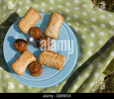 Eine Nahaufnahme von Wurstbrötchen und Schweinefleischpasteten auf einer blauen Platte auf einen grünen Picknickkorb in Somerset, Großbritannien. Stockfoto