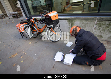 Weiblicher TNT-Postradrundkurier in Uniform mit markengebundener Fahrradsortierpost auf dem Bürgersteig in Central London, Großbritannien. Städtischer Zustelldienst in Aktion. Stockfoto