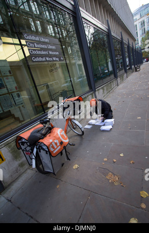 Weiblicher TNT-Postradrundkurier in Uniform mit markengebundener Fahrradsortierpost auf dem Bürgersteig in Central London, Großbritannien. Städtischer Zustelldienst in Aktion. Stockfoto