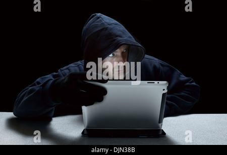Vermummte männliche Vertreter einer Cyber-kriminellen, mit einem Tabletcomputer. Stockfoto